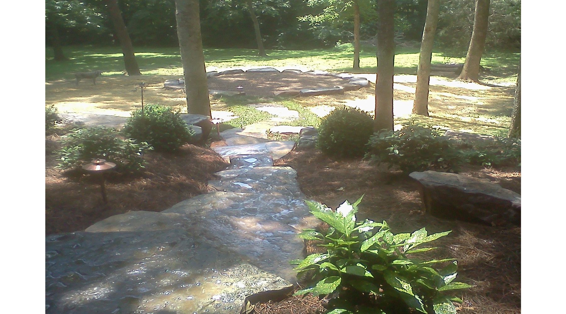 Picture of a stone walkway leading to a round area surrounded by trees.