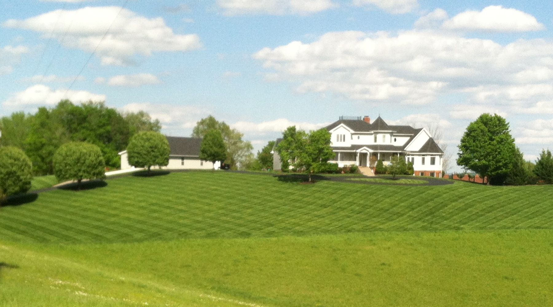 Picture of a large house on a hill with diamond patterns cut into the grass.