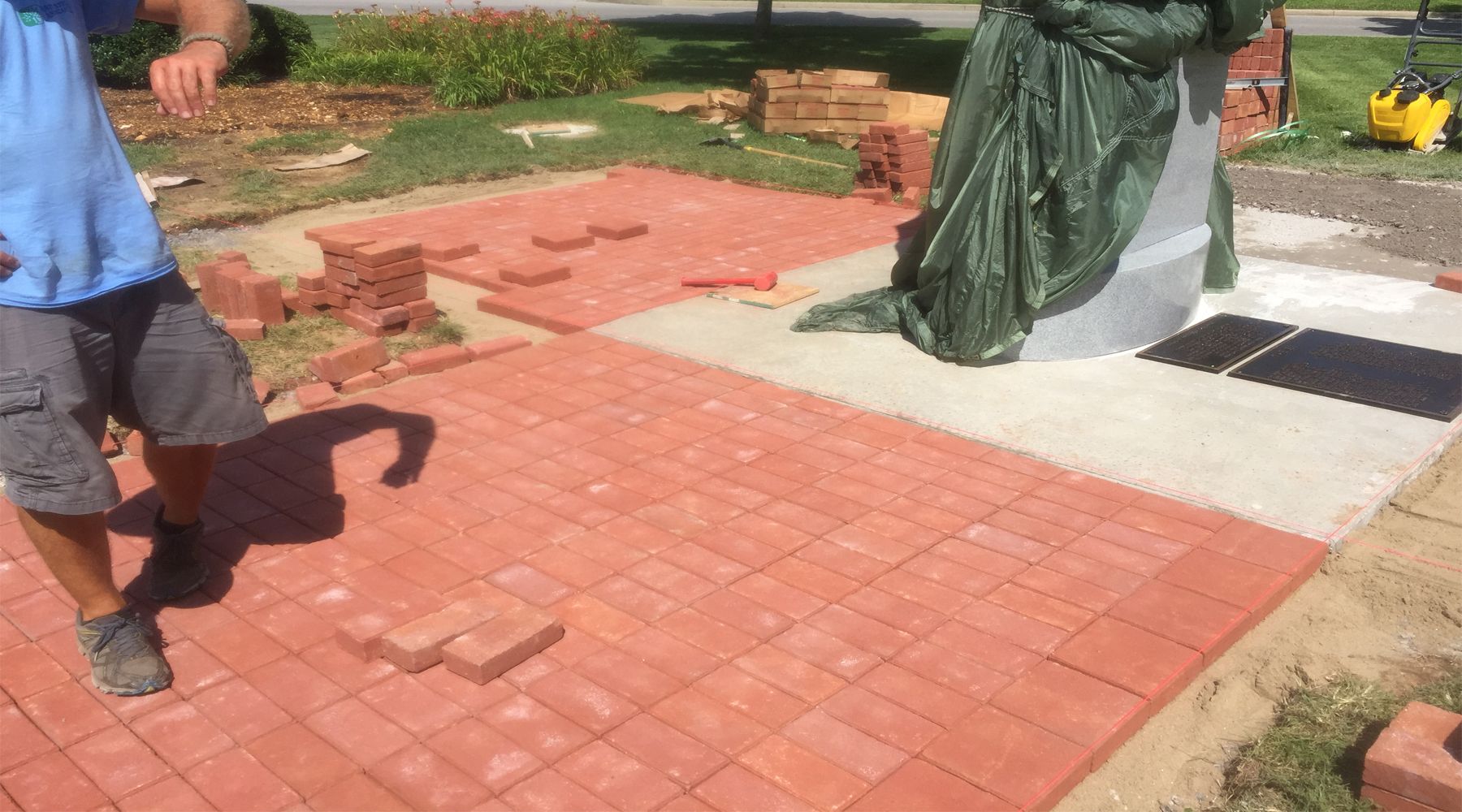 Picture of a man laying a red brick pathway. 
