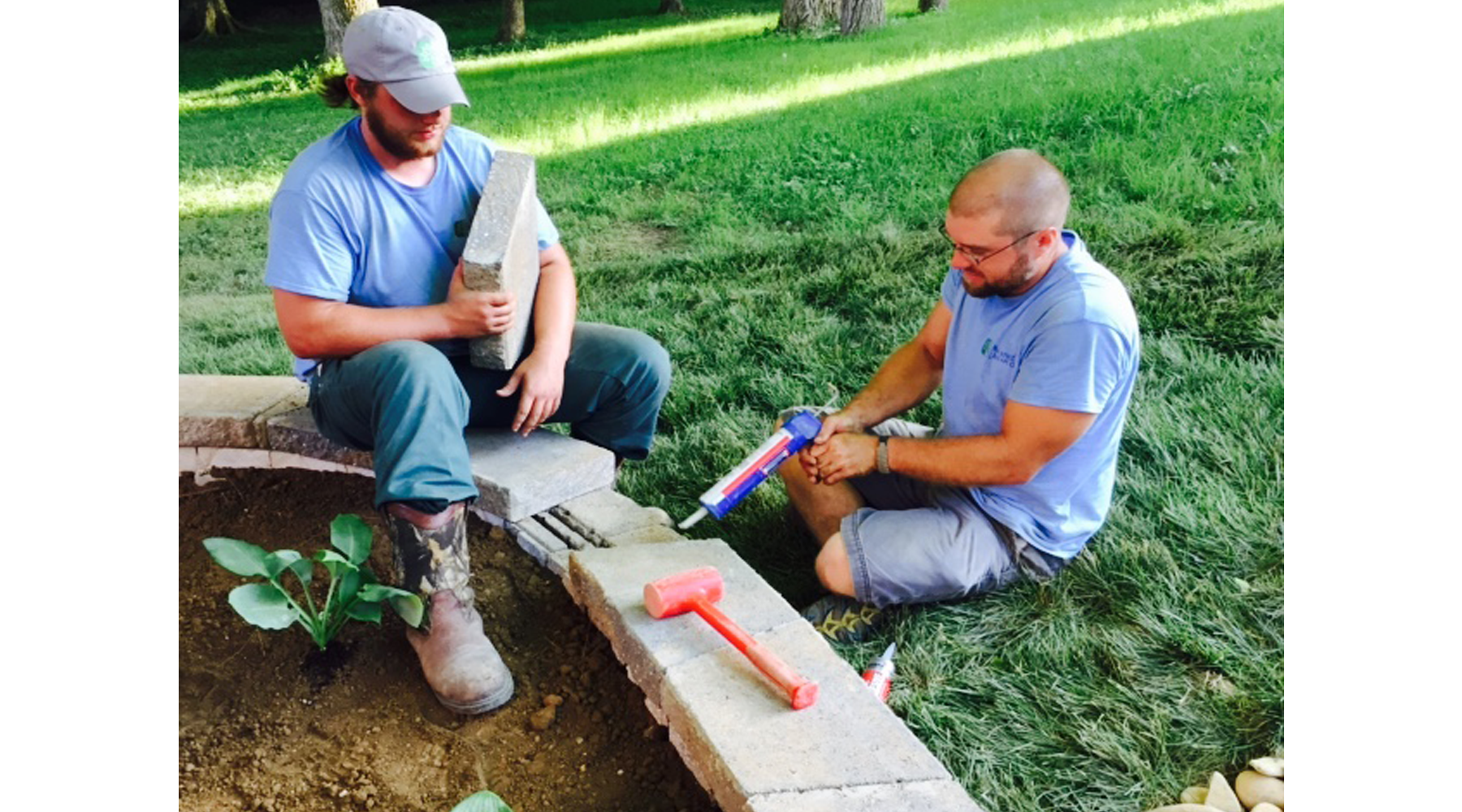 Picture of two men working on the retainer wall of a flower garden.